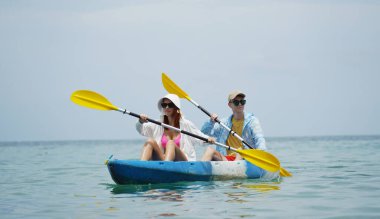 Genç çift, açık mavi bir kanoyla birlikte sarı raketlerle mutlu bir şekilde yol alıyorlar..
