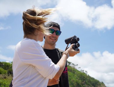 Bir erkek ve bir kadın dikkatle dürbünle uzaktan ilginç bir şeye bakıyorlar..