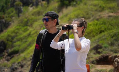 Bir erkek ve bir kadın dikkatle dürbünle uzaktan ilginç bir şeye bakıyorlar..