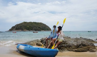 Kumsalda genç bir çift ellerinde kano kürekleri ve suda eğlenceli bir yolculuğa hazırlar..