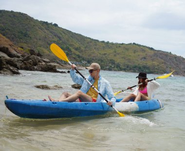 Genç çift, açık mavi bir kanoyla birlikte sarı raketlerle mutlu bir şekilde yol alıyorlar..
