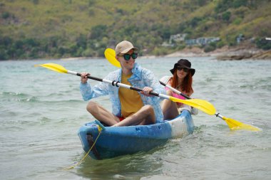 Genç çift, açık mavi bir kanoyla birlikte sarı raketlerle mutlu bir şekilde yol alıyorlar..