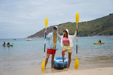 Kumsalda genç bir çift ellerinde kano kürekleri ve suda eğlenceli bir yolculuğa hazırlar..