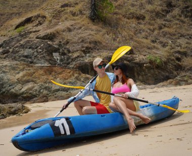 Kumsalda genç bir çift ellerinde kano kürekleri ve suda eğlenceli bir yolculuğa hazırlar..