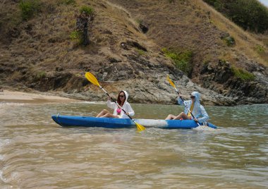Genç çift, açık mavi bir kanoyla birlikte sarı raketlerle mutlu bir şekilde yol alıyorlar..