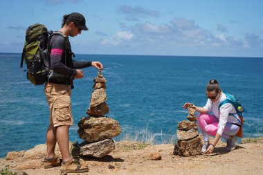 Bir erkek ve bir kadın dikkatle kayaları okyanusa yakın sanatsal bir şekilde istifliyorlar.