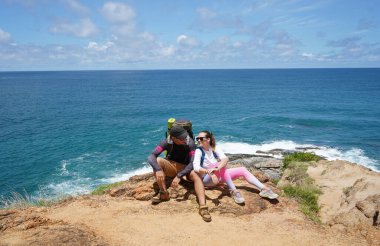 Genç bir çift okyanus manzarası sunan engebeli kayalık bir uçurumda yürüyüş yapıyor..