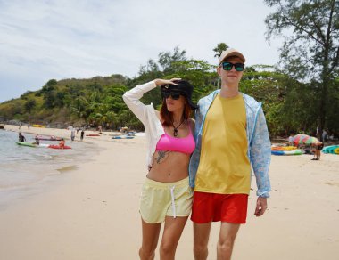 Genç bir çift kumsalda boş boş yürüyor, el ele tutuşuyor ve sıcak güneşin tadını çıkarıyor..