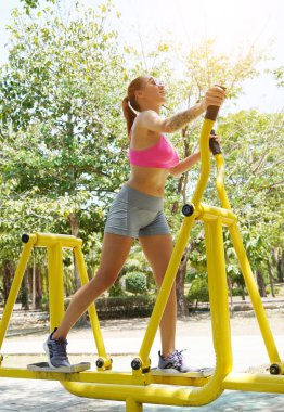 Genç bir kadın parkta bir makinede egzersiz yapıyor..