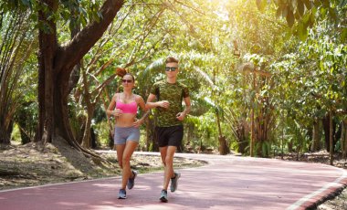 Bir adam ve bir kadın güzel bir parkta birlikte koşuyorlar, temiz havanın tadını çıkarıyorlar.