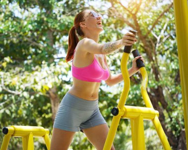 Genç bir kadın parkta bir makinede egzersiz yapıyor..