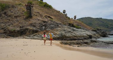 Genç bir çift kumsalda boş boş yürüyor, el ele tutuşuyor ve sıcak güneşin tadını çıkarıyor..