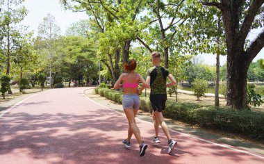 Bir adam ve bir kadın güzel bir parkta birlikte koşuyorlar, temiz havanın tadını çıkarıyorlar.