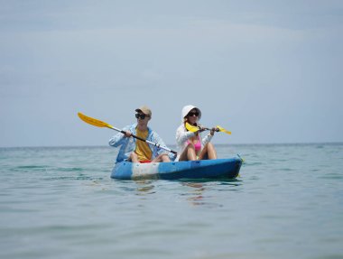 Genç çift, açık mavi bir kanoyla birlikte sarı raketlerle mutlu bir şekilde yol alıyorlar..