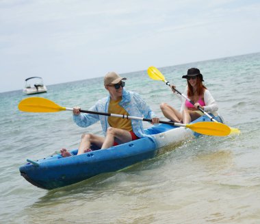 Genç çift, açık mavi bir kanoyla birlikte sarı raketlerle mutlu bir şekilde yol alıyorlar..