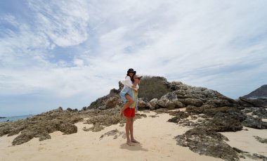 Genç bir çift kumsalda boş boş yürüyor, el ele tutuşuyor ve sıcak güneşin tadını çıkarıyor..