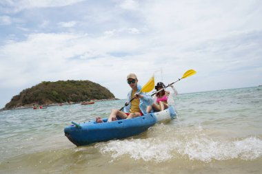 Genç çift, açık mavi bir kanoyla birlikte sarı raketlerle mutlu bir şekilde yol alıyorlar..