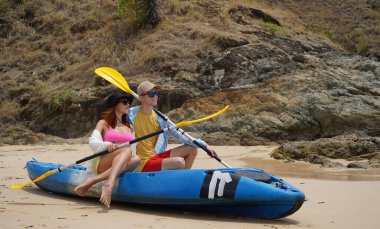 Kumsalda genç bir çift ellerinde kano kürekleri ve suda eğlenceli bir yolculuğa hazırlar..