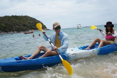 Genç çift, açık mavi bir kanoyla birlikte sarı raketlerle mutlu bir şekilde yol alıyorlar..