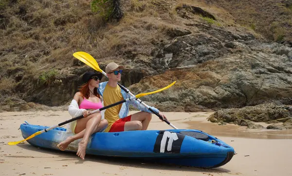 Kumsalda genç bir çift ellerinde kano kürekleri ve suda eğlenceli bir yolculuğa hazırlar..