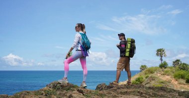 Genç bir çift okyanus manzarası sunan engebeli kayalık bir uçurumda yürüyüş yapıyor..