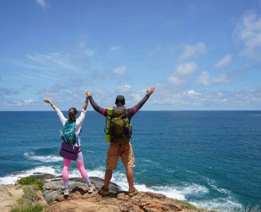Genç bir çift okyanus manzarası sunan engebeli kayalık bir uçurumda yürüyüş yapıyor..