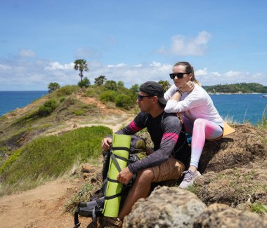Genç bir çift okyanus manzarası sunan engebeli kayalık bir uçurumda yürüyüş yapıyor..