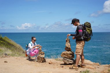 Bir erkek ve bir kadın dikkatle kayaları okyanusa yakın sanatsal bir şekilde istifliyorlar.