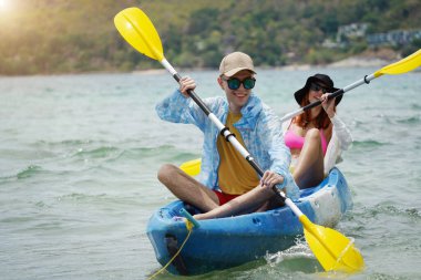 Genç çift, açık mavi bir kanoyla birlikte sarı raketlerle mutlu bir şekilde yol alıyorlar..