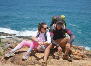 Genç bir çift okyanus manzarası sunan engebeli kayalık bir uçurumda yürüyüş yapıyor..