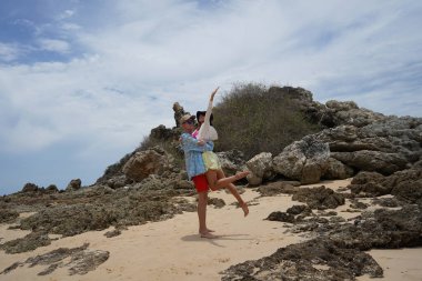 Genç bir çift kumsalda boş boş yürüyor, el ele tutuşuyor ve sıcak güneşin tadını çıkarıyor..