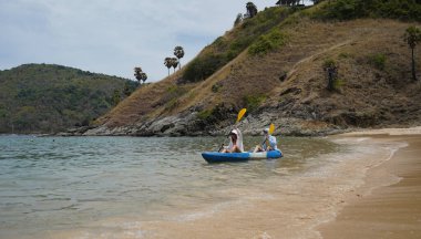 Genç çift, açık mavi bir kanoyla birlikte sarı raketlerle mutlu bir şekilde yol alıyorlar..