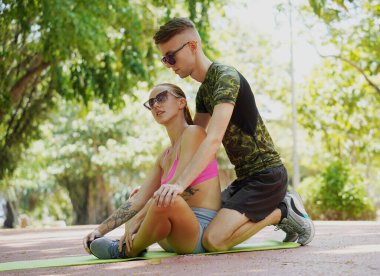 Renkli bir yoga minderinde bacaklarını açarken bir erkek bir kadına yardım ediyor..