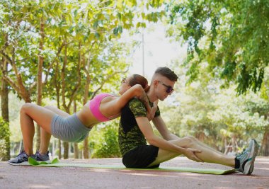 Renkli bir yoga minderinde bacaklarını açarken bir erkek bir kadına yardım ediyor..