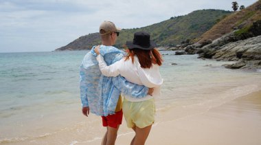 Genç bir çift kumsalda boş boş yürüyor, el ele tutuşuyor ve sıcak güneşin tadını çıkarıyor..