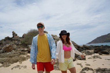 Genç bir çift kumsalda boş boş yürüyor, el ele tutuşuyor ve sıcak güneşin tadını çıkarıyor..