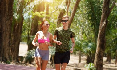 Bir adam ve bir kadın güzel bir parkta birlikte koşuyorlar, temiz havanın tadını çıkarıyorlar.