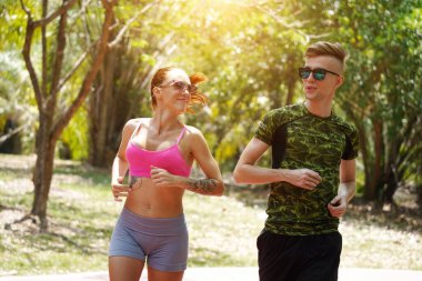 Bir adam ve bir kadın güzel bir parkta birlikte koşuyorlar, temiz havanın tadını çıkarıyorlar.