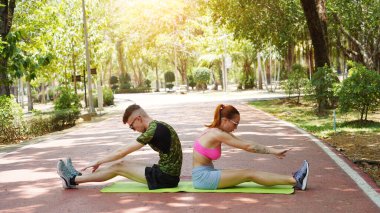 Renkli bir yoga minderinde bacaklarını açarken bir erkek bir kadına yardım ediyor..