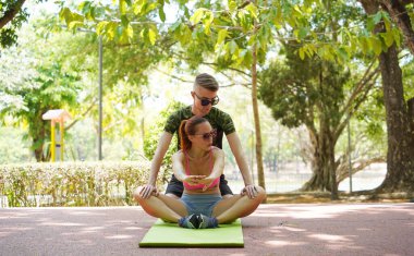 Renkli bir yoga minderinde bacaklarını açarken bir erkek bir kadına yardım ediyor..
