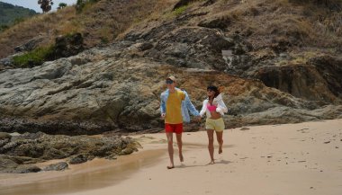 Genç bir çift kumsalda boş boş yürüyor, el ele tutuşuyor ve sıcak güneşin tadını çıkarıyor..