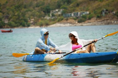Genç çift, açık mavi bir kanoyla birlikte sarı raketlerle mutlu bir şekilde yol alıyorlar..