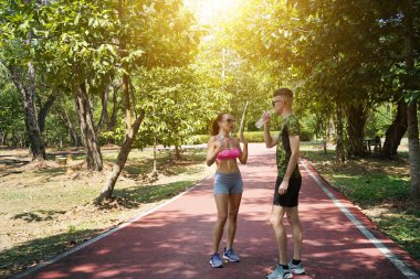 Bir adam ve bir kadın parkta birlikte koştuktan sonra şişelerden ferahlatıcı su içiyorlar..