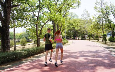 Bir adam ve bir kadın güzel bir parkta birlikte koşuyorlar, temiz havanın tadını çıkarıyorlar.