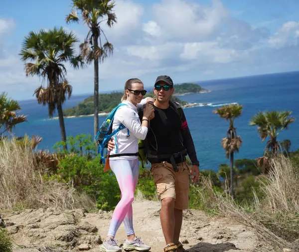 Genç bir çift okyanus manzarası sunan engebeli kayalık bir uçurumda yürüyüş yapıyor..