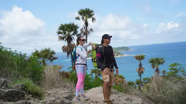 Genç bir çift okyanus manzarası sunan engebeli kayalık bir uçurumda yürüyüş yapıyor..