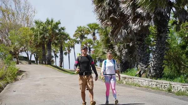 Bir erkek ve bir kadın, doğa güzelliği ve sükunetle çevrili bir yolda rahatça yürüyorlar..