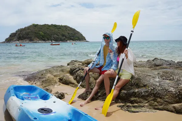 Kumsalda genç bir çift ellerinde kano kürekleri ve suda eğlenceli bir yolculuğa hazırlar..