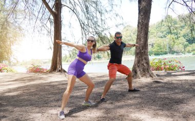 Bir adam ve bir kadın parkta birlikte esneme egzersizleri yapıyorlar..