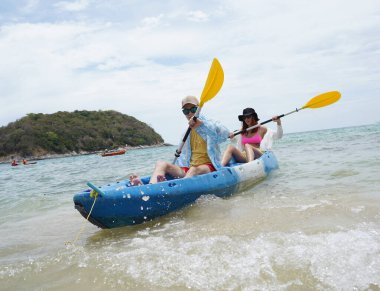 Genç çift, açık mavi bir kanoyla birlikte sarı raketlerle mutlu bir şekilde yol alıyorlar..